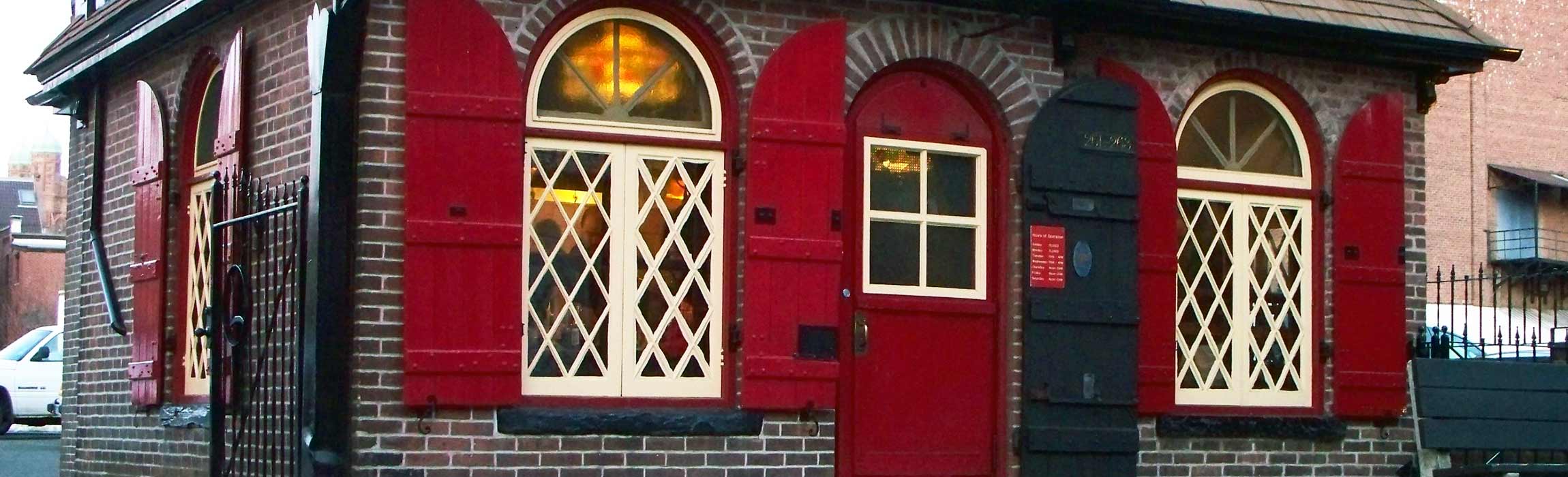 Brick exterior of Louis' Lunch restaurant in New Haven, CT with red barn door shutters